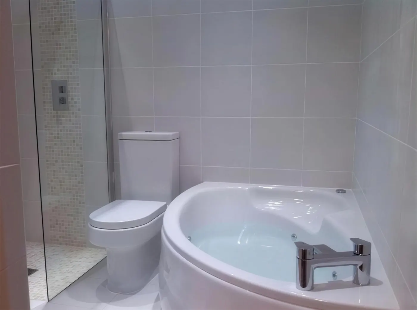 Corner bath and tiled bathroom with a glazed shower screen